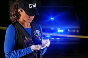 A CSI female standing next to a police car with blue lights